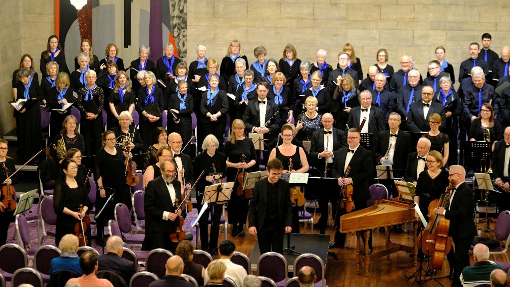 Choir and orchestra, standing in front of audience.